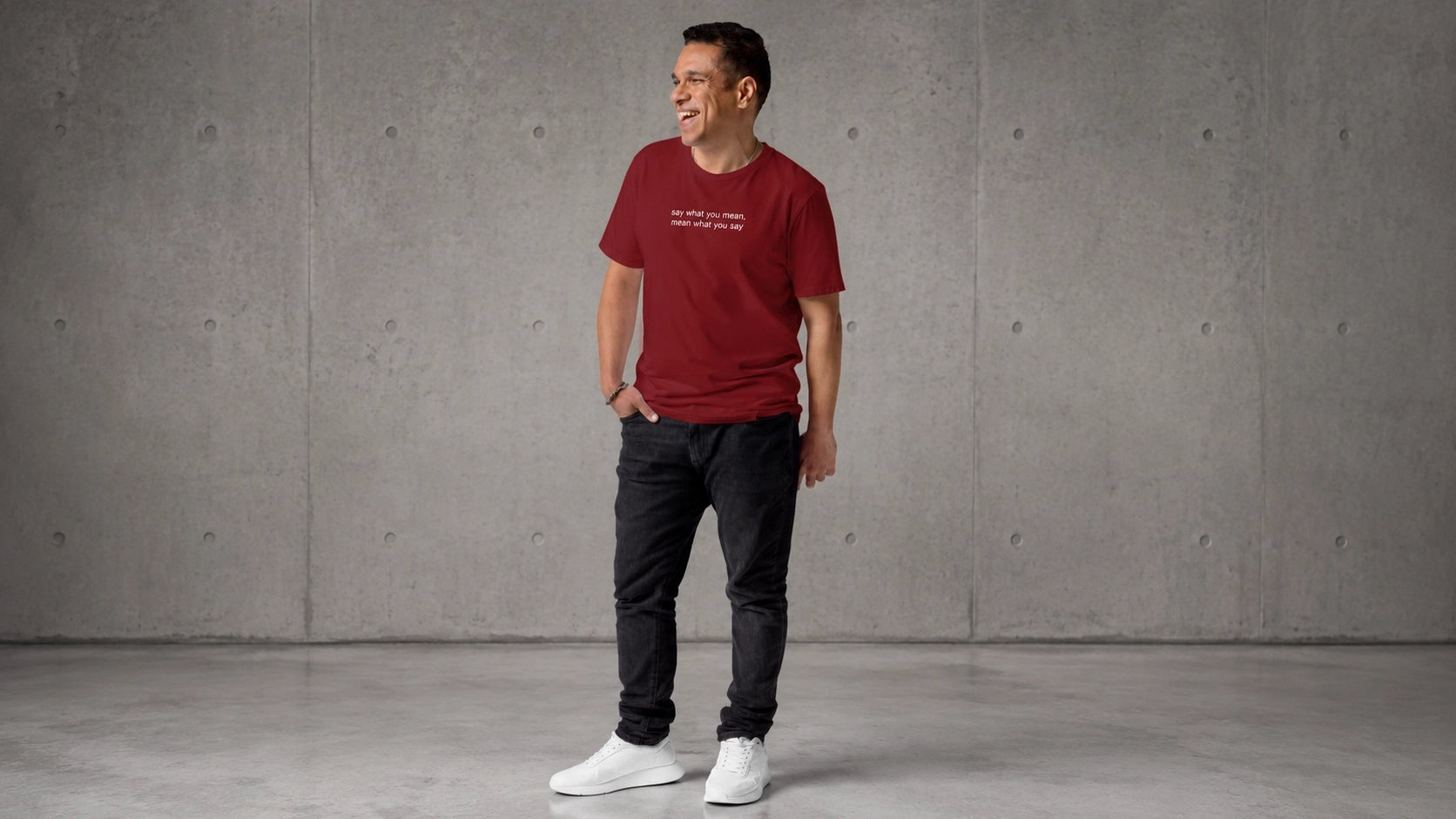 Man wearing a say what you mean t-shirt standing against a gray concrete wall.